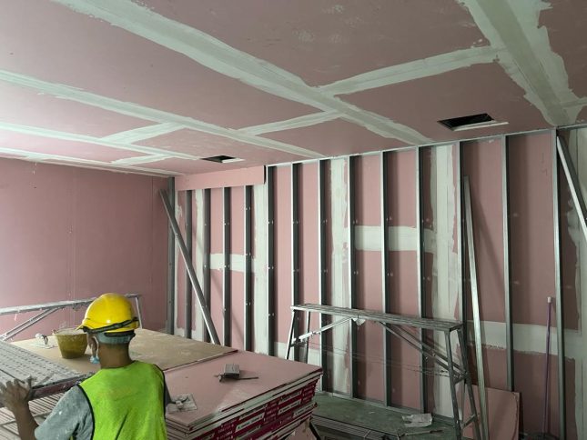 Ongoing drywall partition works with the ceiling framework and a worker on-site during renovation.