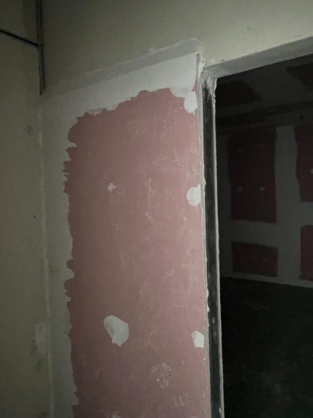 Close-up of drywall partition with plastered joints and door frame installation in progress.