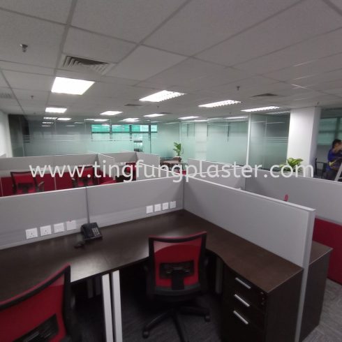 Cubicle row with desks, red chairs, and glass wall in background.