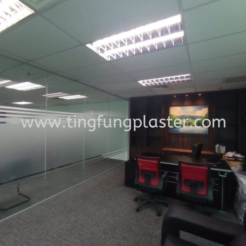 Larger office space with glass partition, desks, and black-and-red chairs.