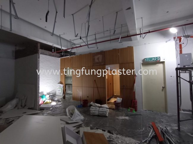 Exposed ceiling wiring, scattered tools, and a temporary partition wall with an EXIT sign