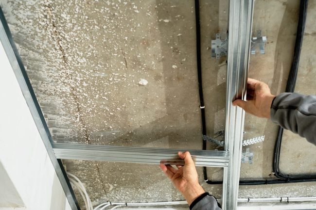 Worker installing standard drywall panels on a basic metal stud frame.