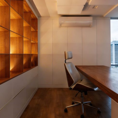Modern office interior with minimalist wooden shelving, ambient lighting, and a sleek desk with chair.