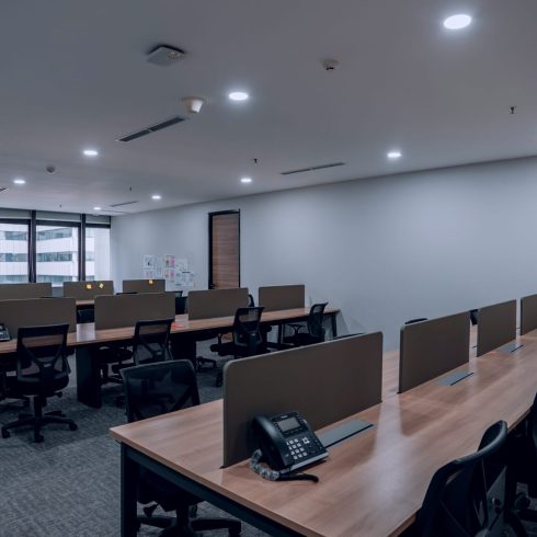 Office workspace-with long wooden desks partitioned workstations and black chairs scaled