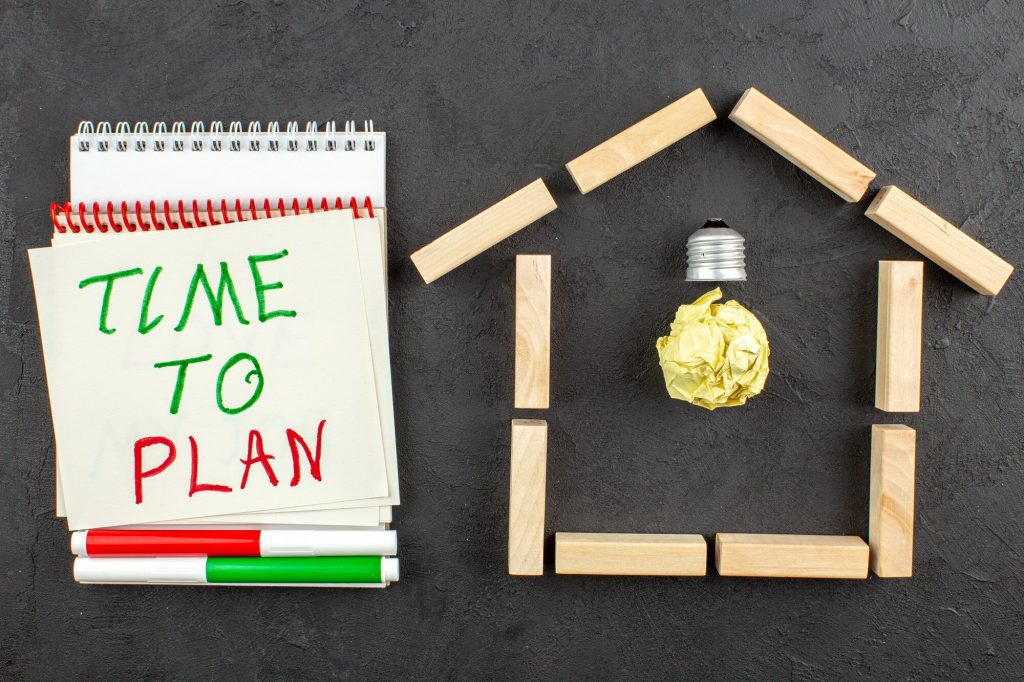 top view idea light bulb house shaped wood blocks time plan written notepad red green markers black